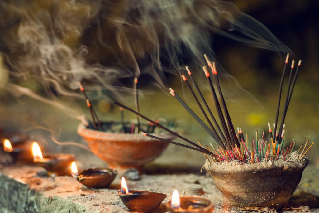 Incense sticks and oil lamps emit smoke and light, creating a serene, spiritual atmosphere.