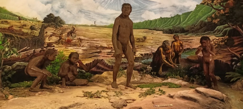 Life-sized sculptures of prehistoric humans in a lush, detailed landscape, showcasing early human activity and environment.