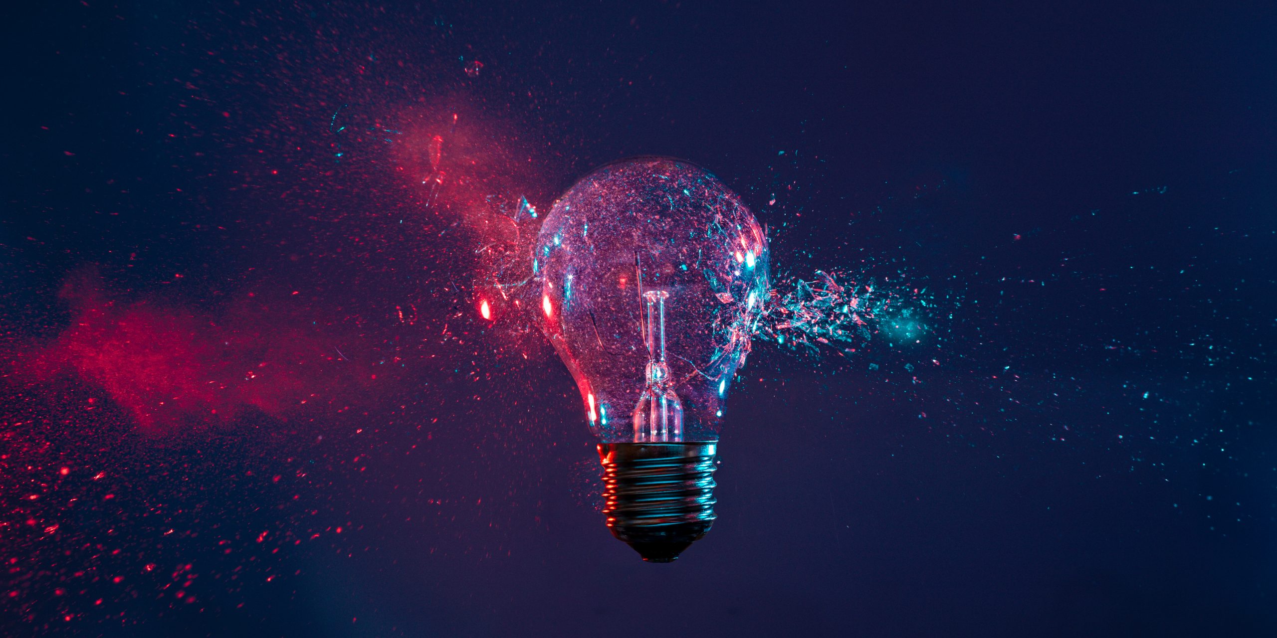 A light bulb shatters, surrounded by colorful splashes of blue and pink, creating a dynamic, energetic scene.