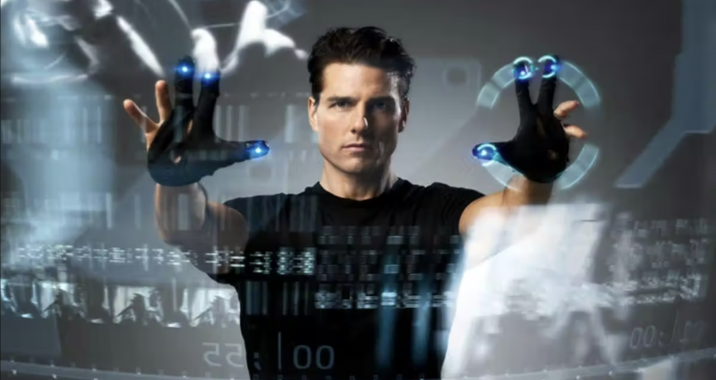 A man in a black shirt uses futuristic gloves to interact with holographic displays.