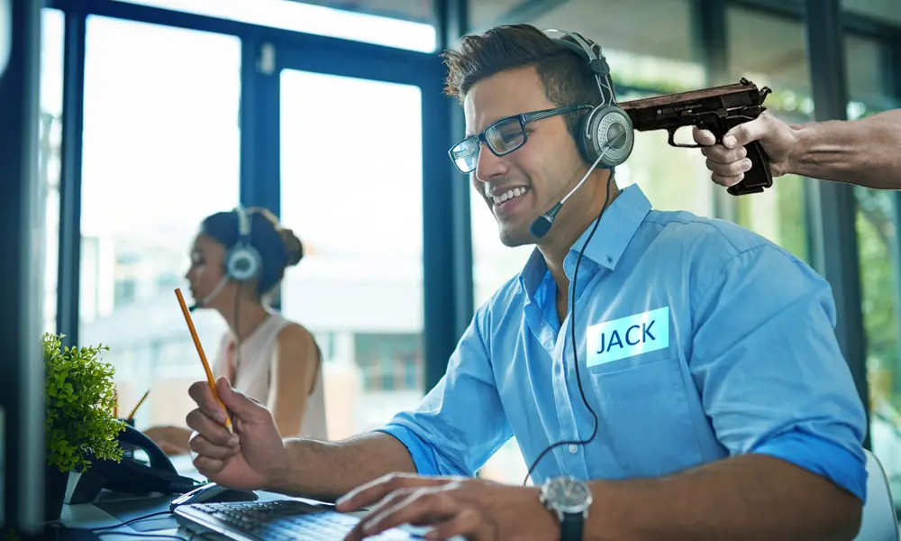 A man in a headset smiles while a hand holds a gun behind him, creating a tense contrast in the office setting.