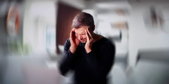 A man with short hair holds his head in distress, conveying a sense of frustration or pain in a blurred background.