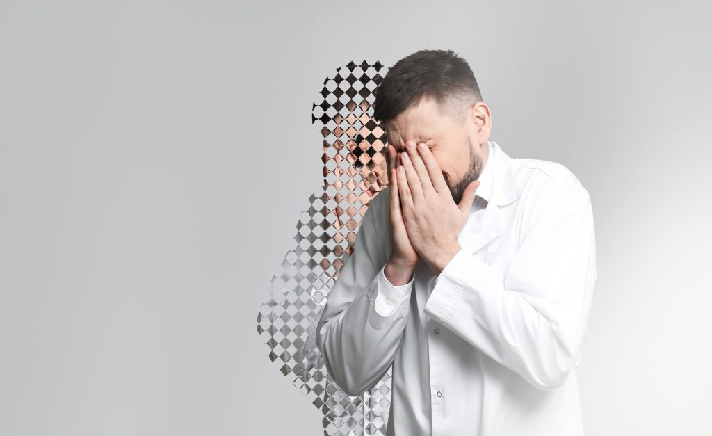 A man in a white lab coat covers his face, blending into a pixelated background, conveying a sense of distress.
