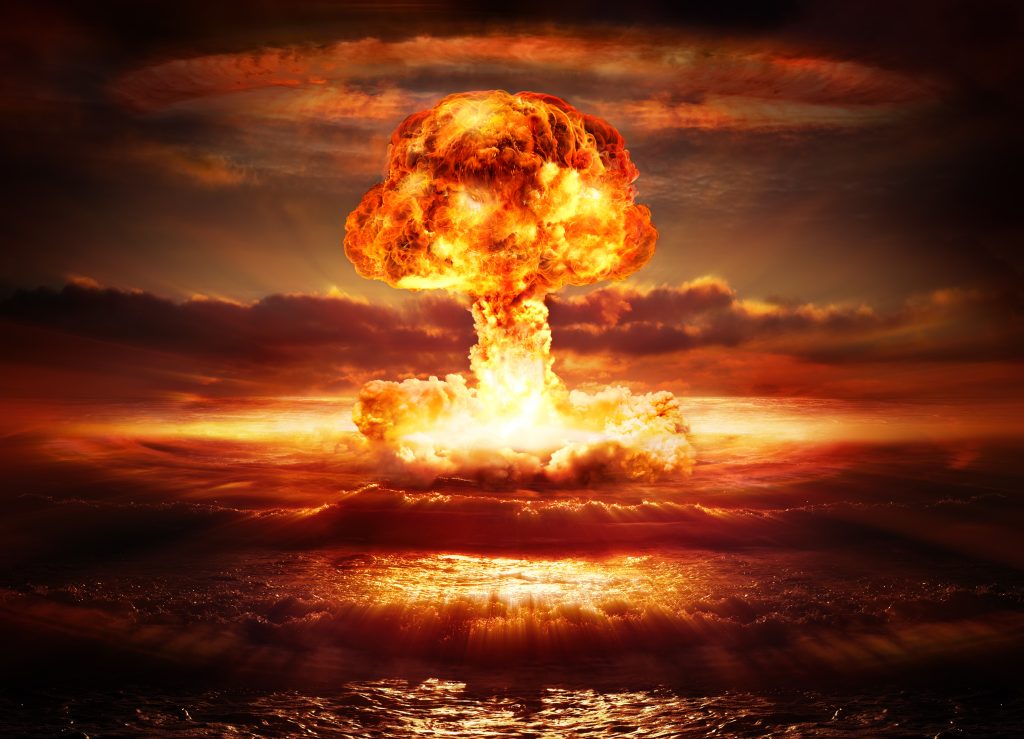 A massive nuclear explosion erupts over the ocean, casting an orange glow against dark, swirling clouds.