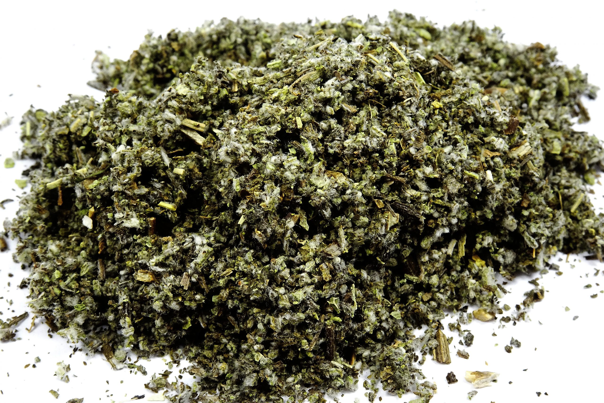 A mound of finely ground green herbal material, with a mix of leaves and stems, set against a white background.