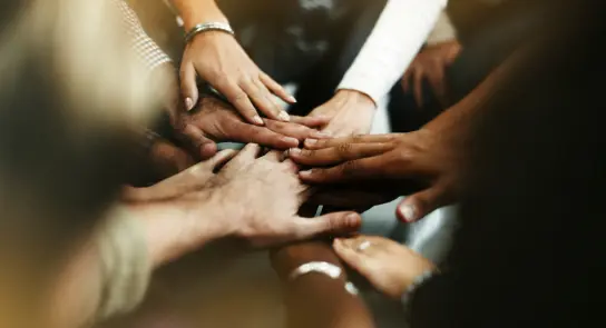 Multiple hands of diverse individuals stacked together in a show of unity and collaboration.