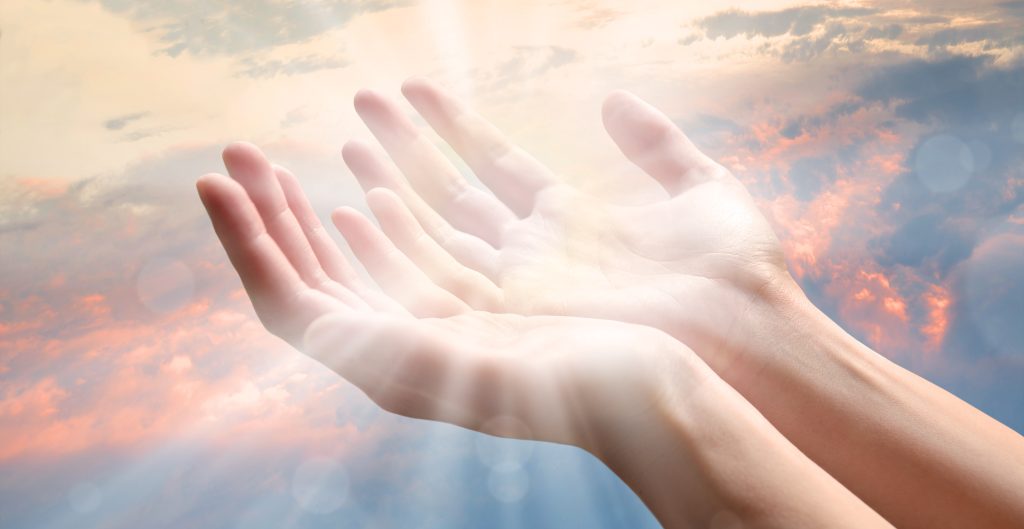 Outstretched hands illuminated by soft light against a cloudy sky, suggesting hope and openness.