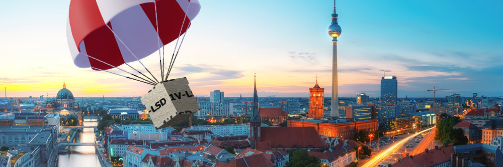 A parachute descends over Berlin, carrying a package, with city skyline and sunset in the background.
