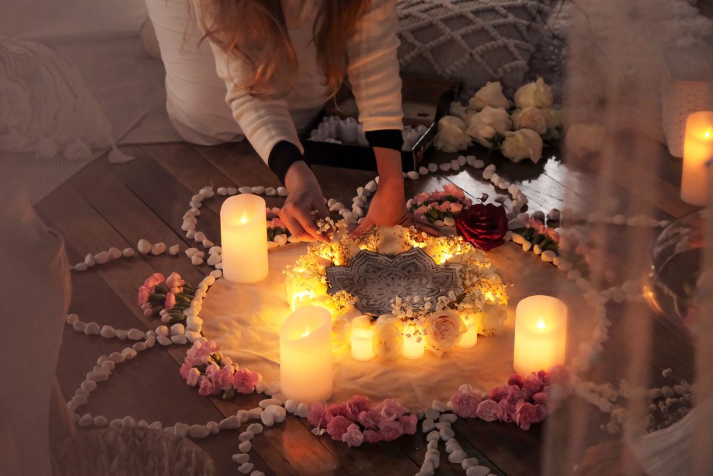 A person arranging flowers and candles in a circular pattern on a wooden floor, creating a serene, illuminated atmosphere.