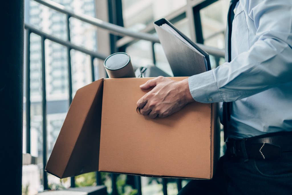 A person in a blue shirt carries a cardboard box and a folder while ascending stairs.