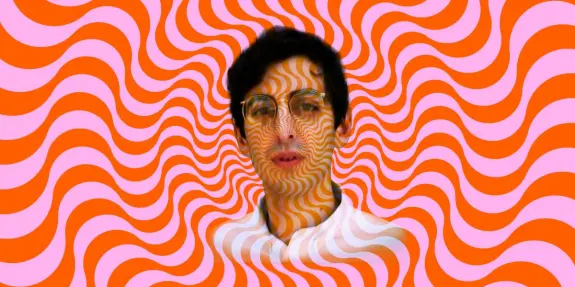 A person with glasses against a vibrant, swirling orange and pink background, creating a hypnotic effect.