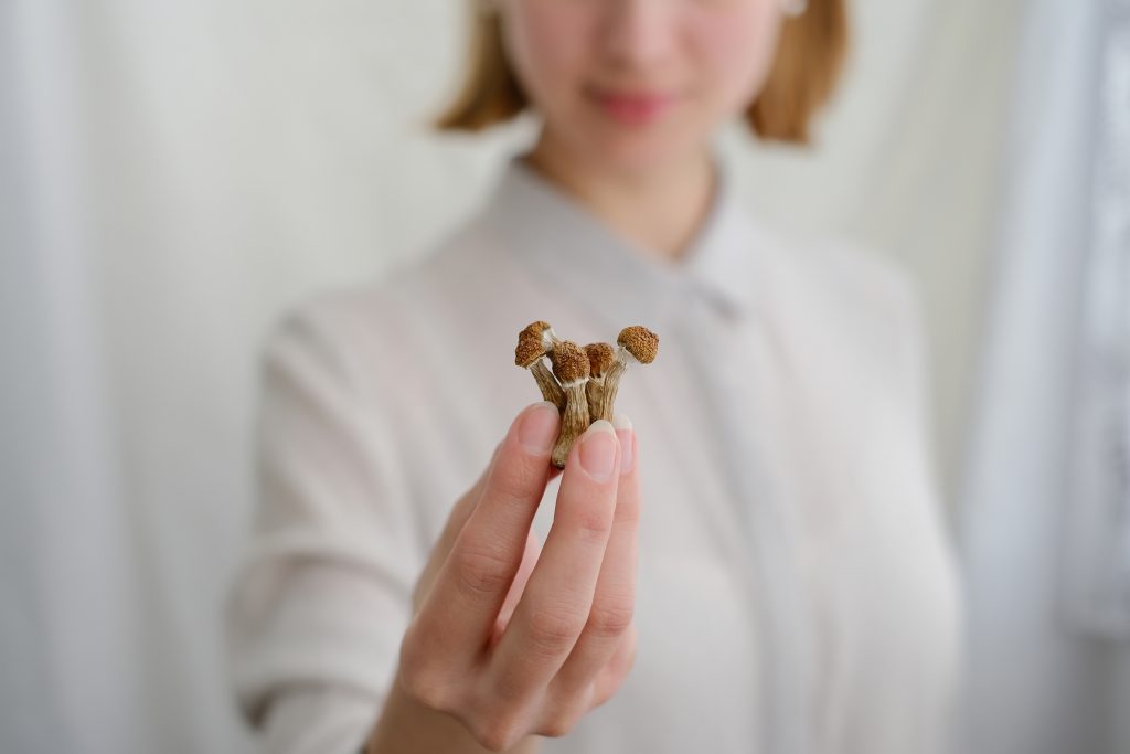 A person holds a small cluster of mushrooms in front of a light background, wearing a light-colored shirt.