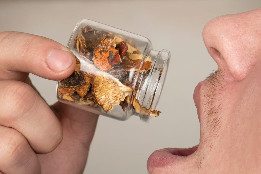 A person holds a small jar filled with dried herbs near their open mouth, ready to consume the contents.