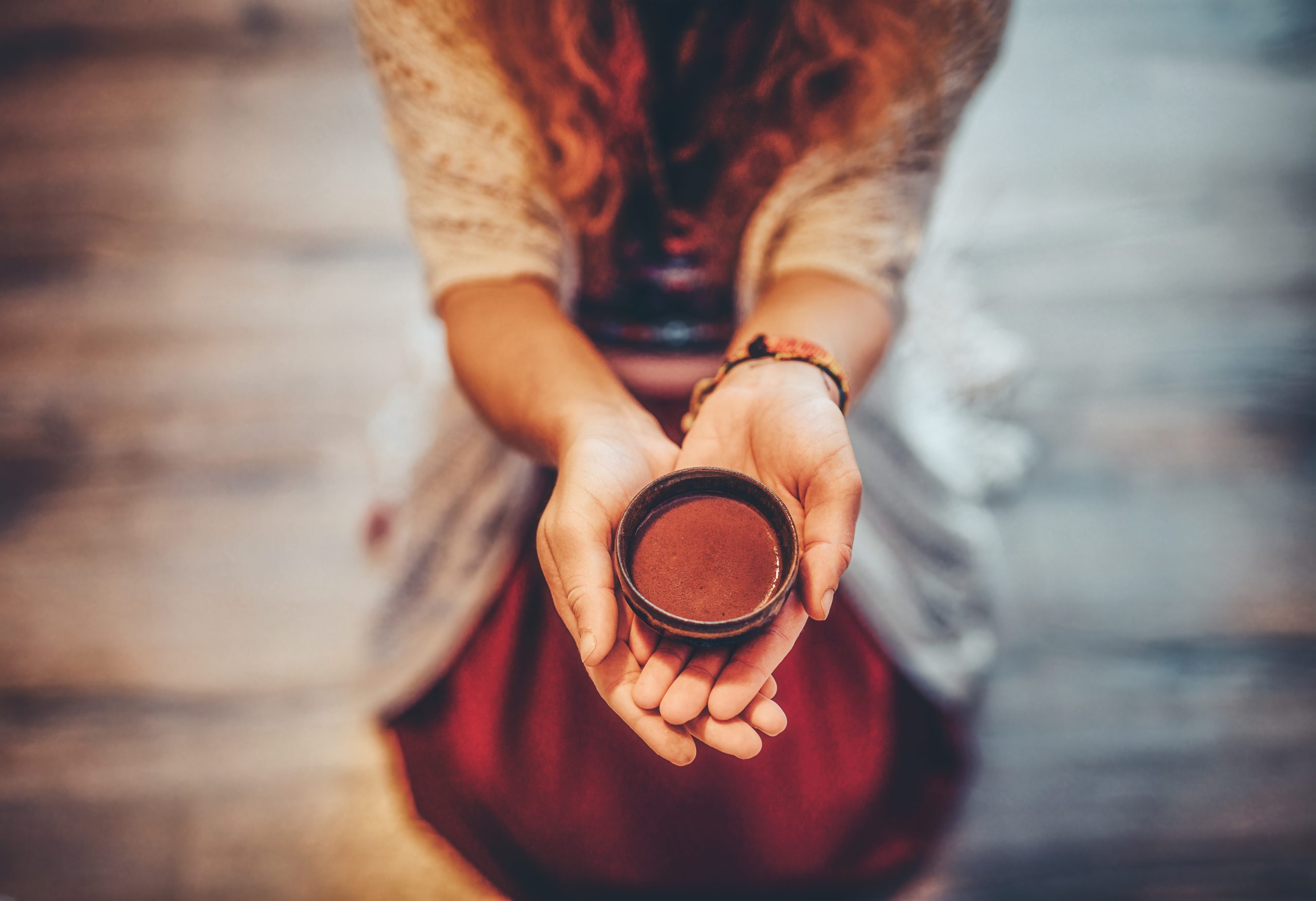 A person holds a small, round bowl in their hands, with a soft focus on their warm, textured clothing.