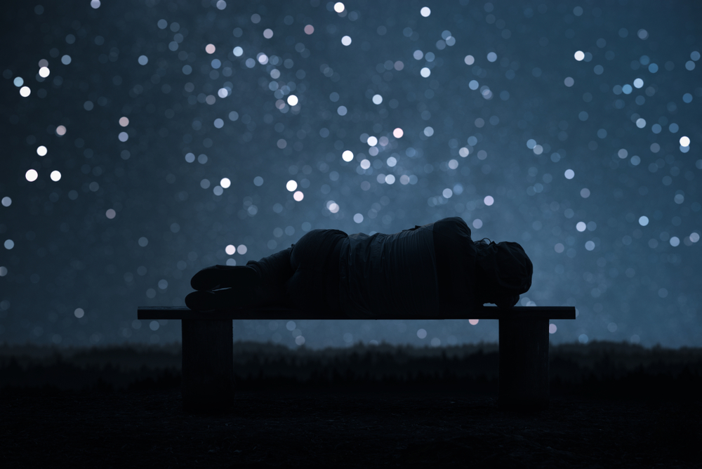 A person lies on a bench under a starry night sky, silhouetted against a backdrop of twinkling stars.
