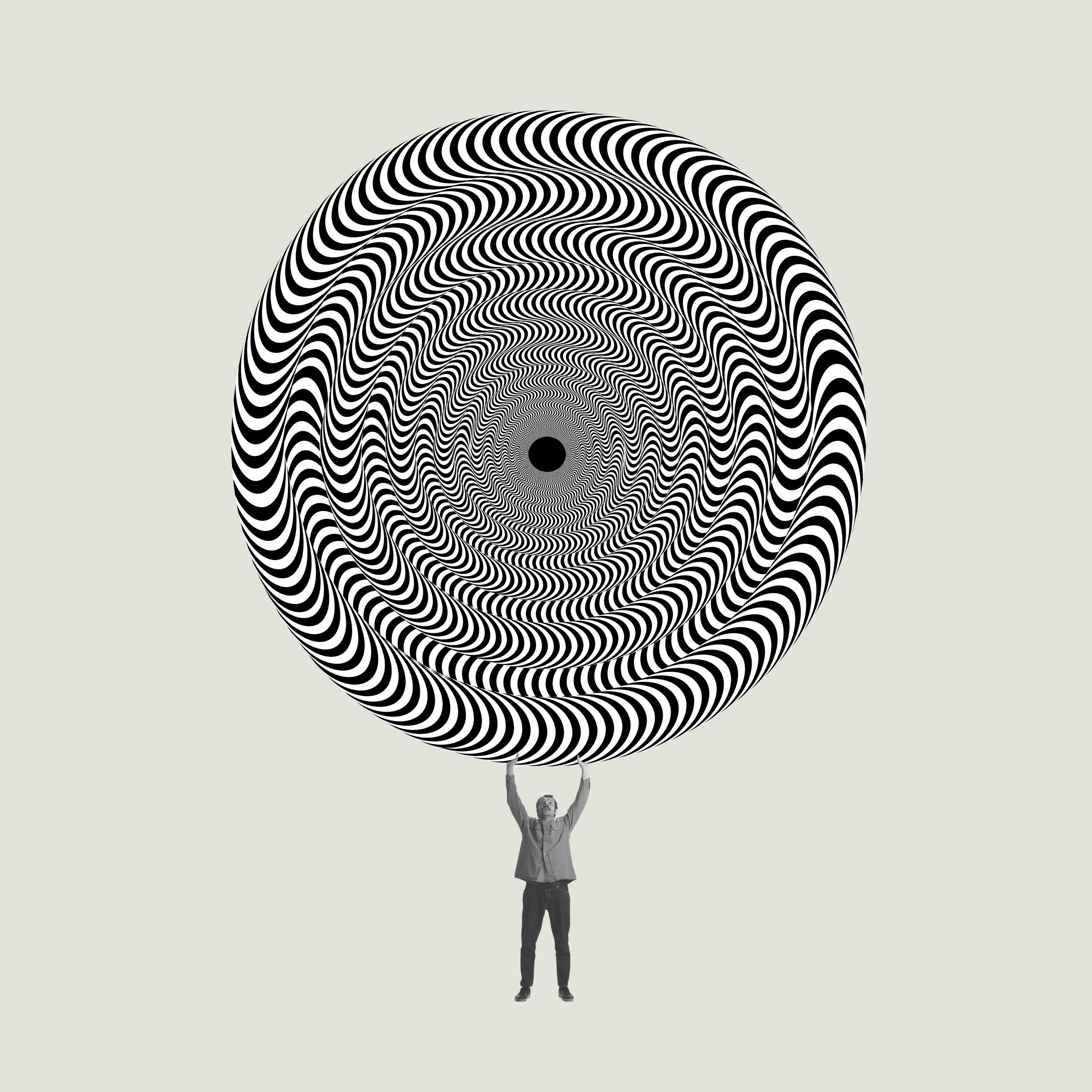 A person lifts a large, swirling black and white spiral pattern, creating a striking optical illusion.