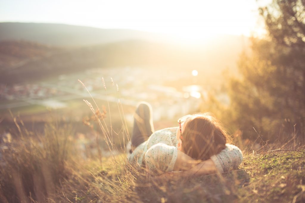 A person relaxes on a hillside, basking in the warm glow of sunset, overlooking a valley and distant hills.