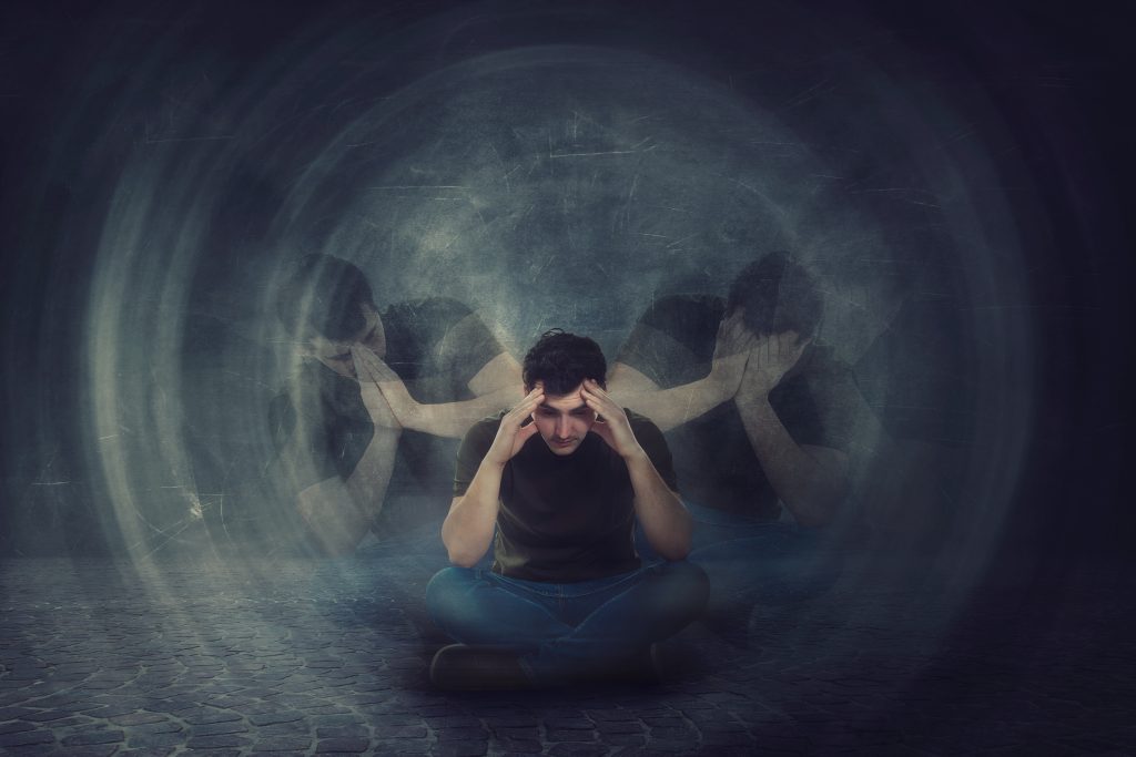 A person sits on the ground, holding their head in distress, surrounded by swirling shadows representing turmoil.