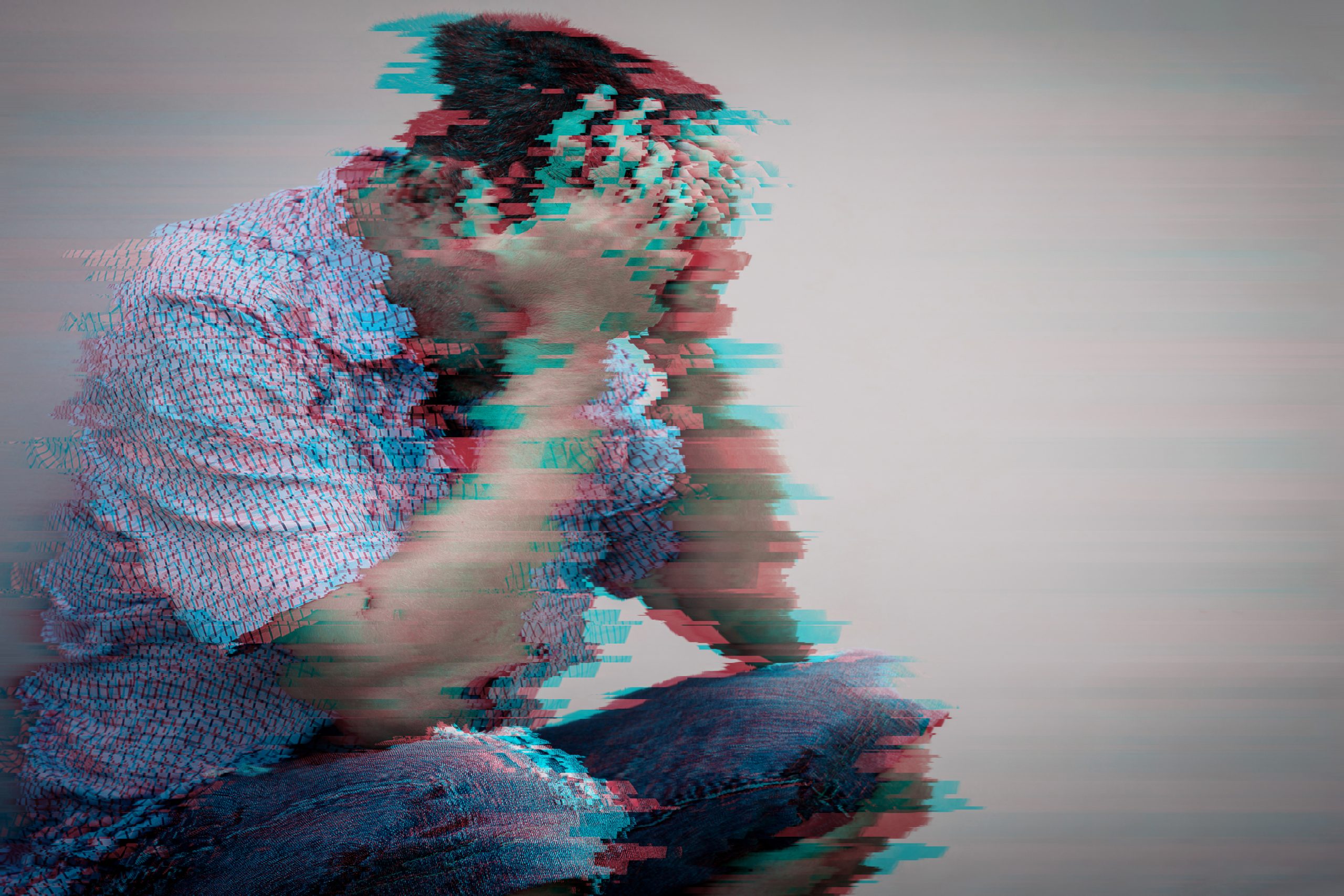 A person sits with their head in their hands, surrounded by a distorted, glitchy effect, conveying distress.