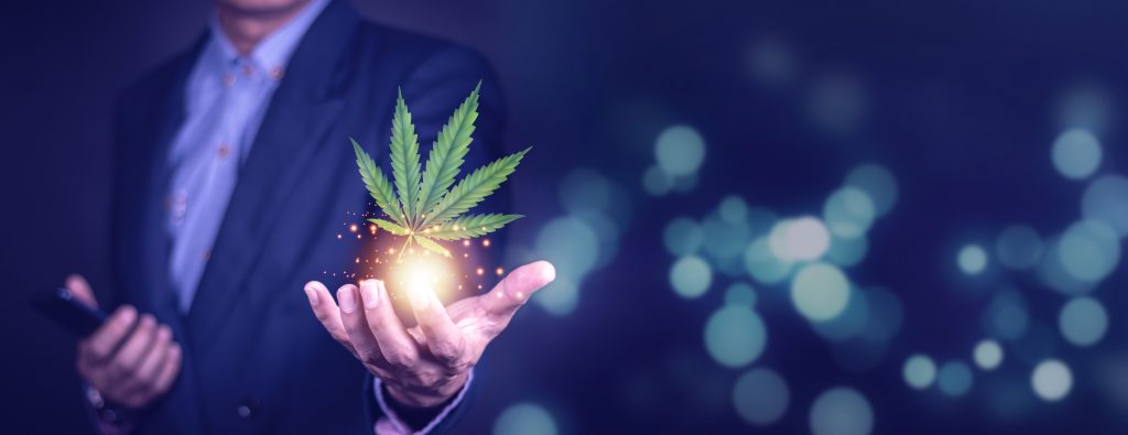 A person in a suit holds a glowing cannabis leaf, surrounded by a blurred, colorful background.