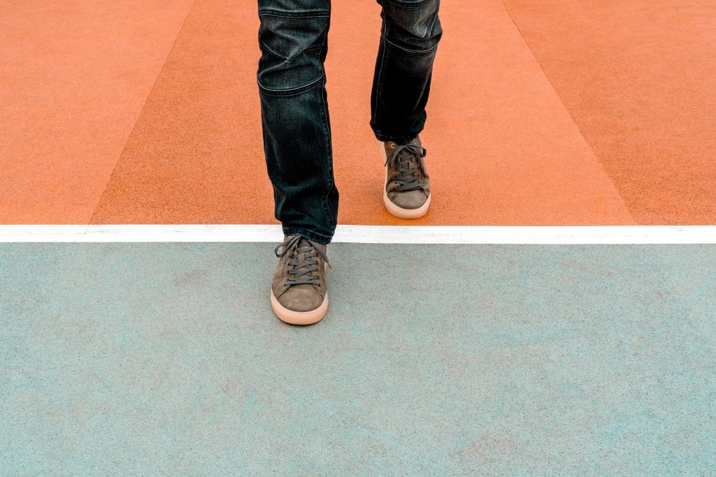 A person walks on a colorful court, with orange and teal sections and a white line dividing them.