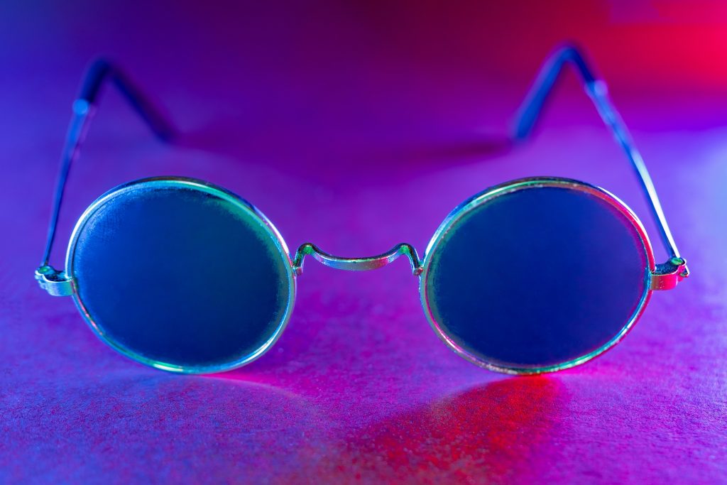 Round, metallic sunglasses with dark lenses, set against a colorful, illuminated background.