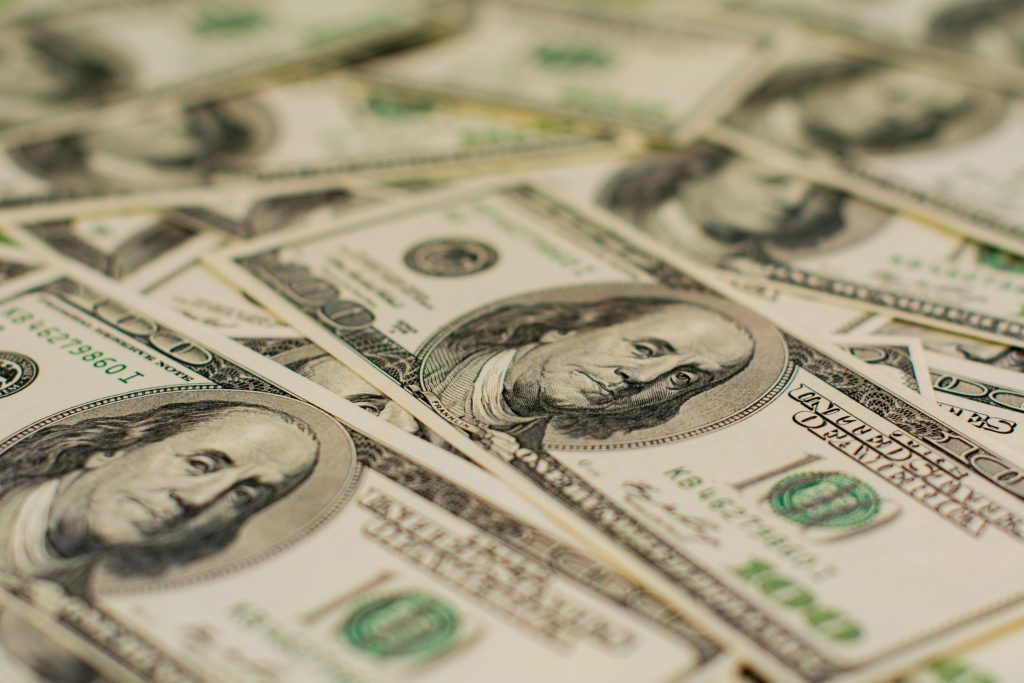 Scattered hundred-dollar bills with detailed portraits and green accents.