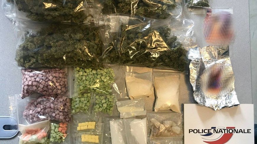 Seized drugs displayed in clear bags, including cannabis, pills, and powdered substances, with a police logo in the corner.