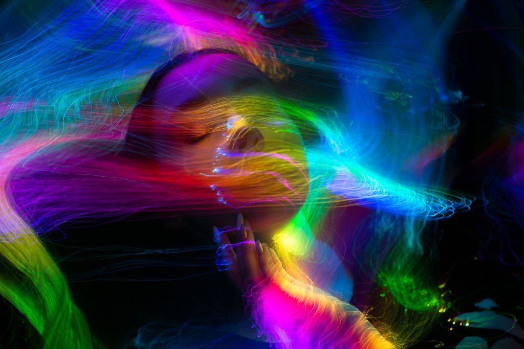 A serene face surrounded by vibrant, swirling neon lights, creating a dreamlike, ethereal atmosphere.