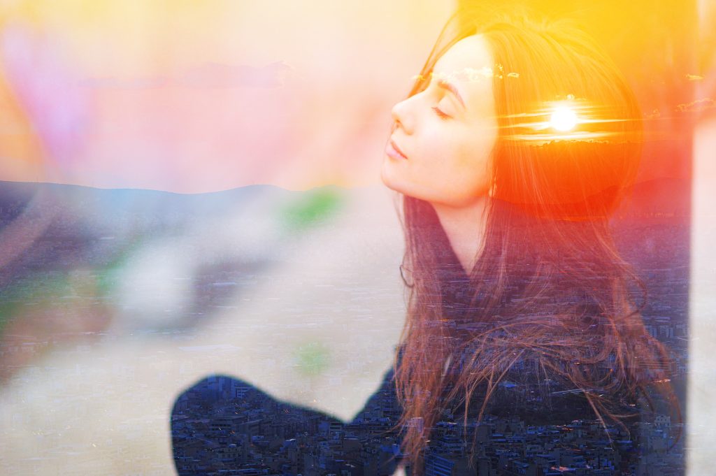 A serene woman with closed eyes, bathed in warm sunset light, blending with a cityscape background.