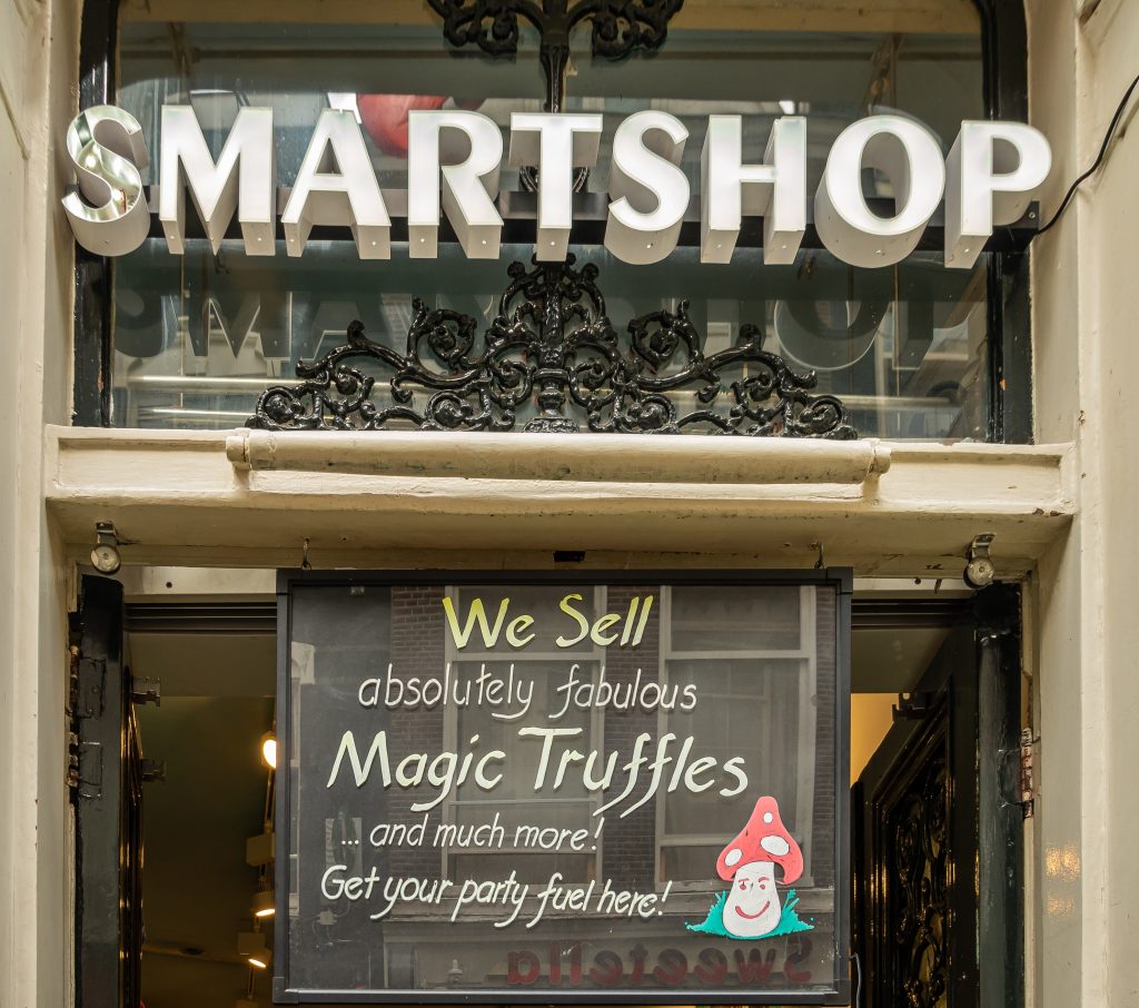 Sign for "SMARTSHOP" above a storefront, featuring a colorful advertisement for magic truffles and party supplies.