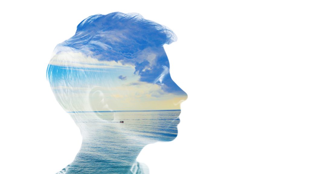 Silhouette of a boy's profile filled with a serene ocean and cloudy sky, blending nature and human form.