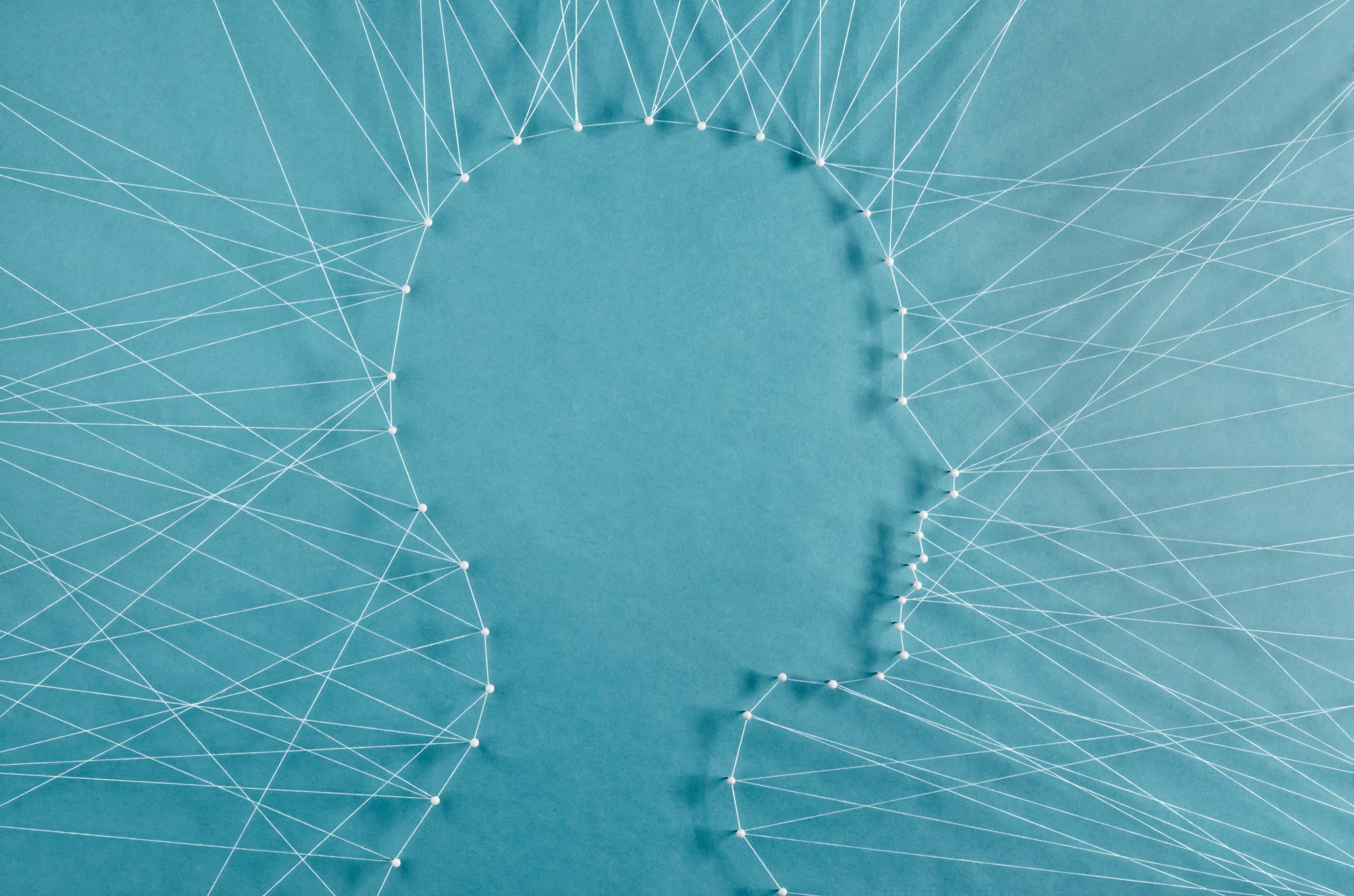 Silhouette of a head outlined with white string and pins on a blue background, symbolizing thoughts or connections.