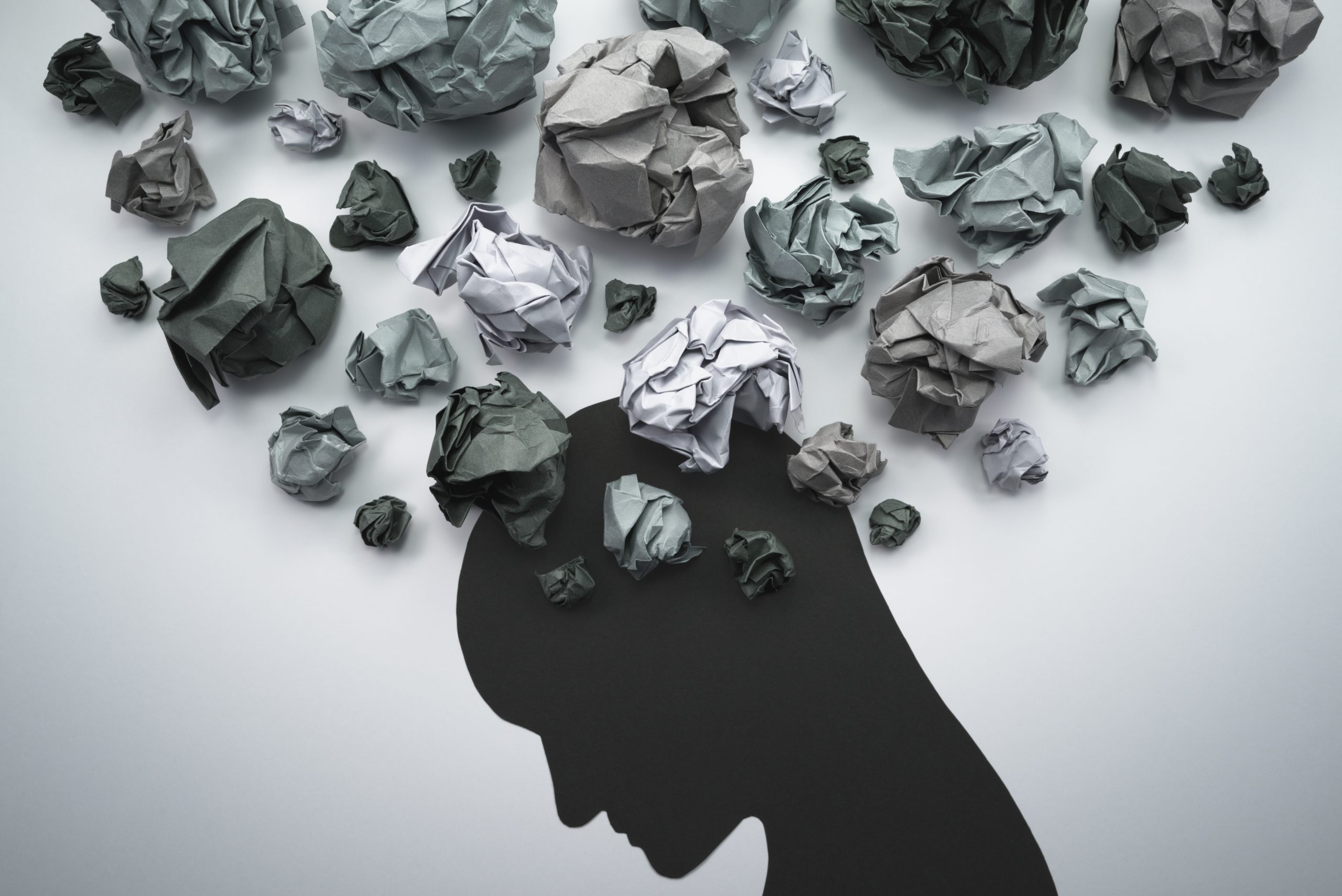 Silhouette of a head surrounded by crumpled paper balls, symbolizing chaotic thoughts or mental clutter.