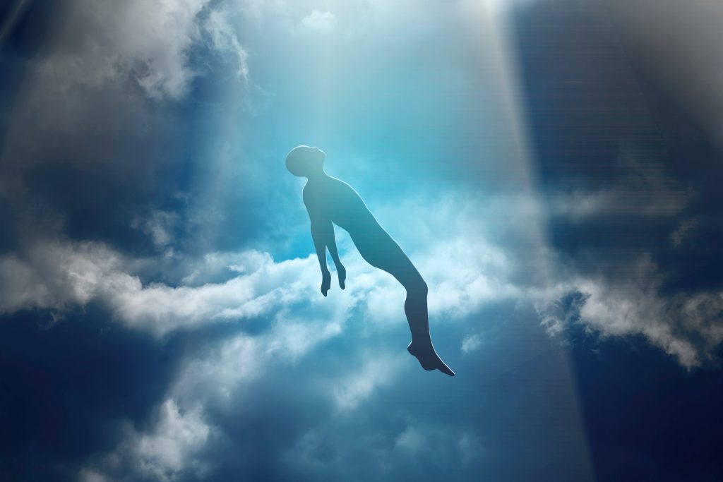 A silhouette of a person floating amidst bright clouds and beams of light in a serene sky.