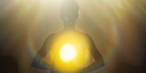 Silhouette of a person with hands clasped, surrounded by a glowing golden light and soft lens flares.