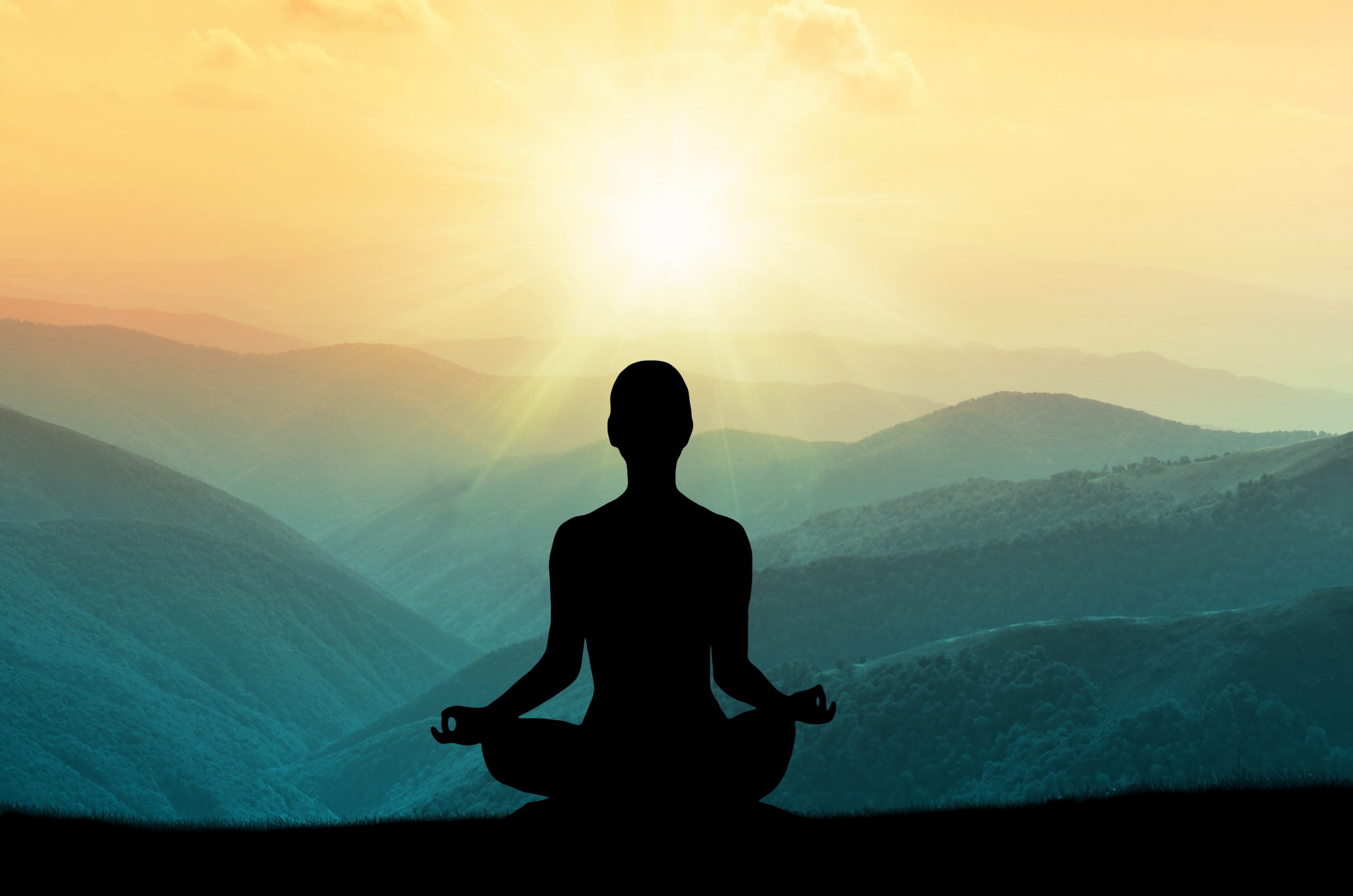Silhouette of a person meditating against a vibrant sunset over rolling mountains.
