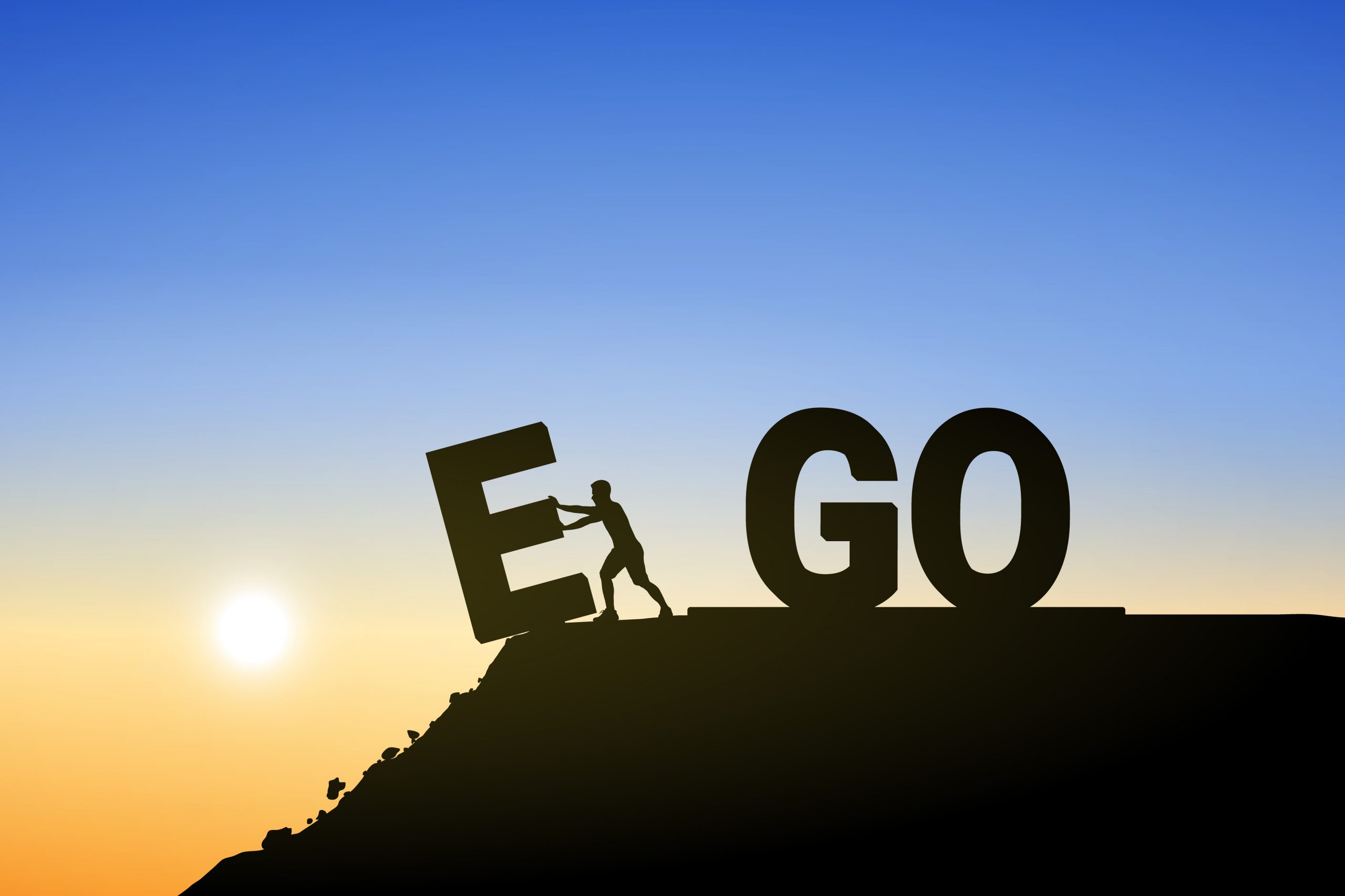 Silhouette of a person pushing the letters "E" and "GO" against a sunset backdrop, symbolizing overcoming ego.