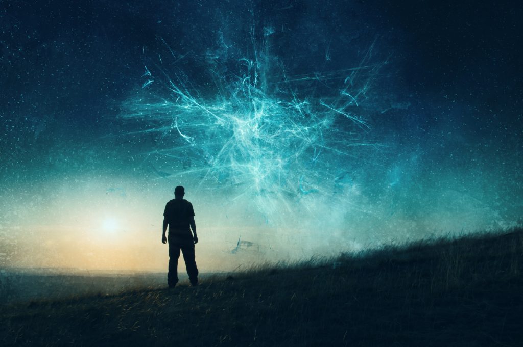 Silhouette of a person standing on a hill, gazing at a starry sky with swirling blue light patterns.