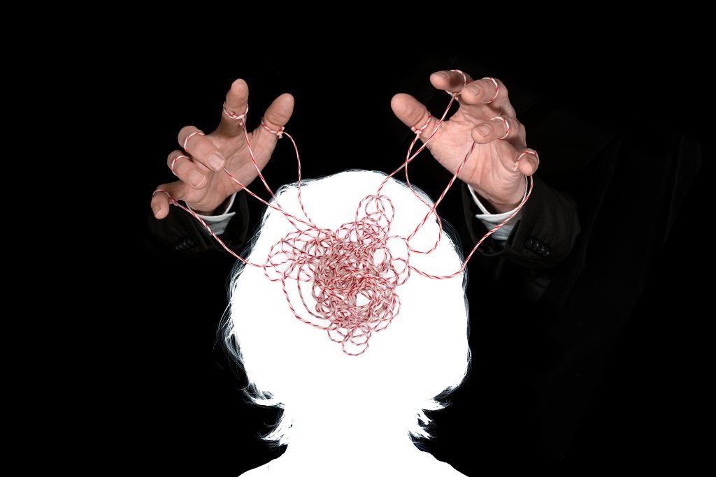 A silhouette of a person with tangled string above their head, hands manipulating the chaotic threads against a black back...