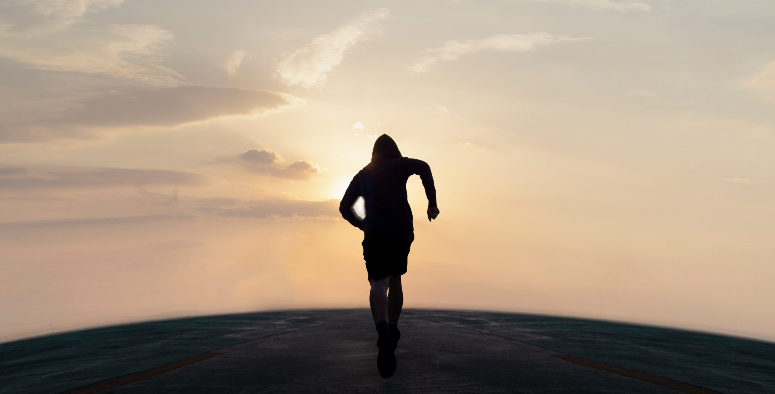 Silhouette of a runner against a sunset, with soft clouds and a warm glow illuminating the horizon.