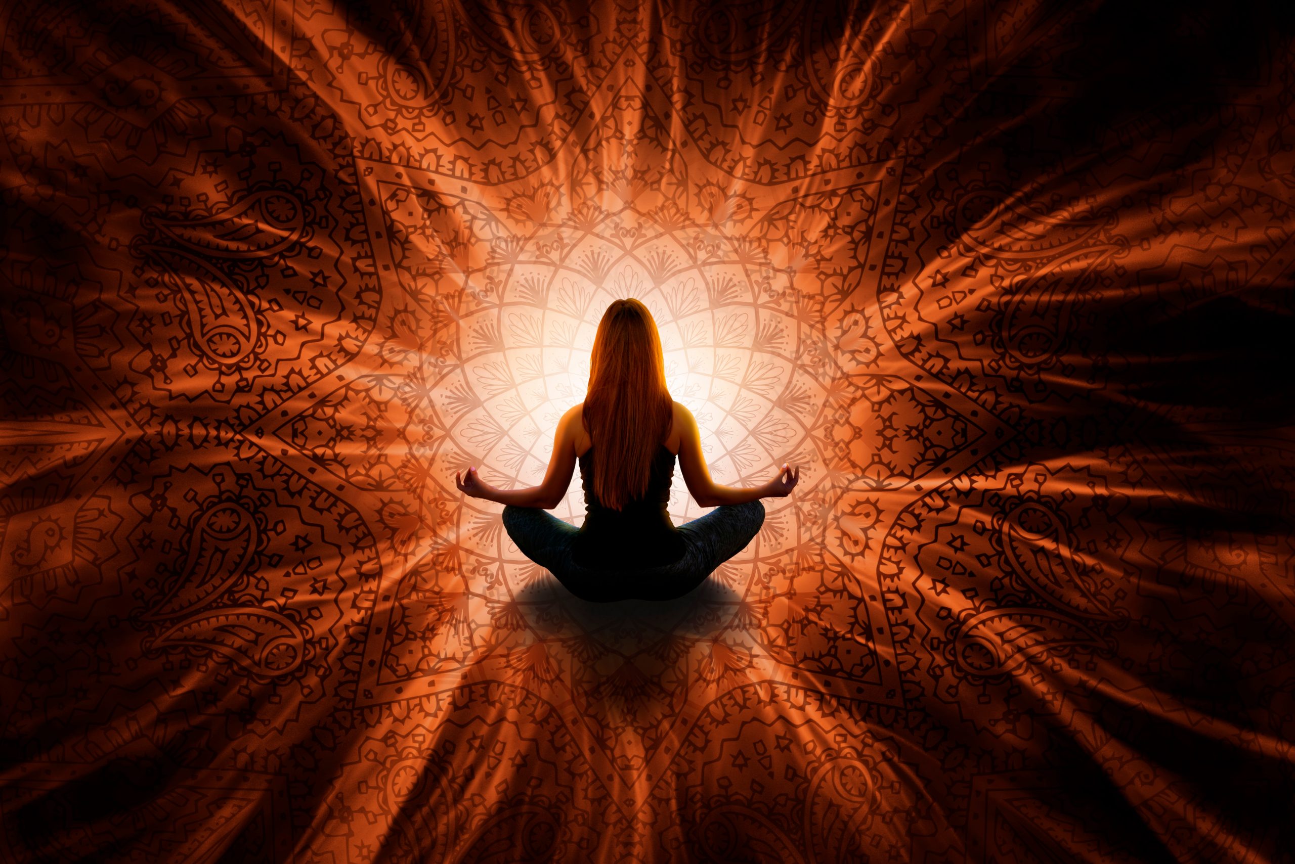 Silhouette of a woman meditating against a vibrant, intricate mandala backdrop, radiating warm orange light.