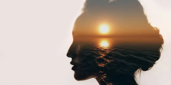 Silhouette of a woman's profile blended with a sunset over the ocean, creating a serene, dreamlike effect.