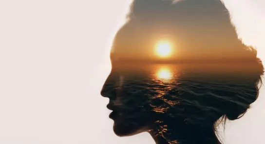 Silhouette of a woman's profile blended with a sunset over the ocean, creating a serene, dreamlike effect.