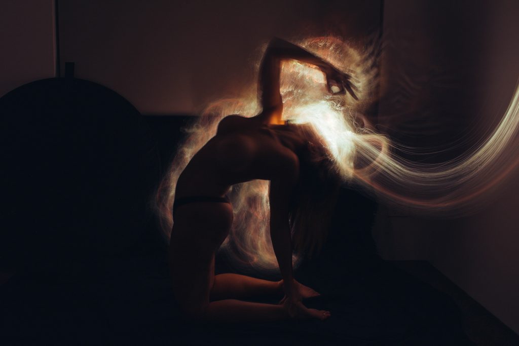 A silhouetted figure in a dark room, arching back with flowing light trails emanating from their head.