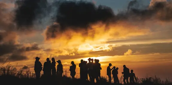 Silhouetted figures against a vibrant sunset, with clouds creating a dramatic sky.