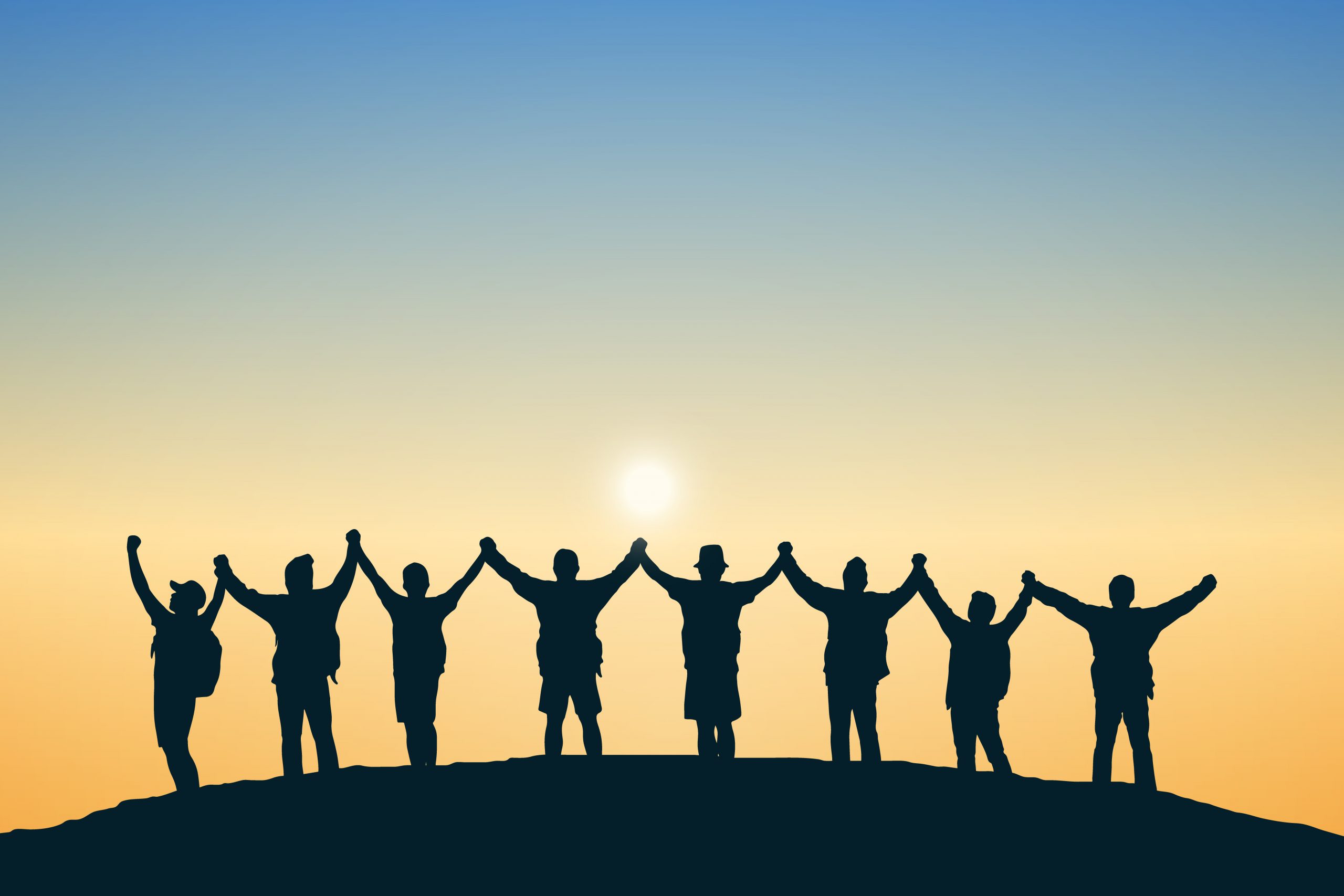 Silhouetted figures holding hands against a sunset, celebrating unity and togetherness on a hilltop.