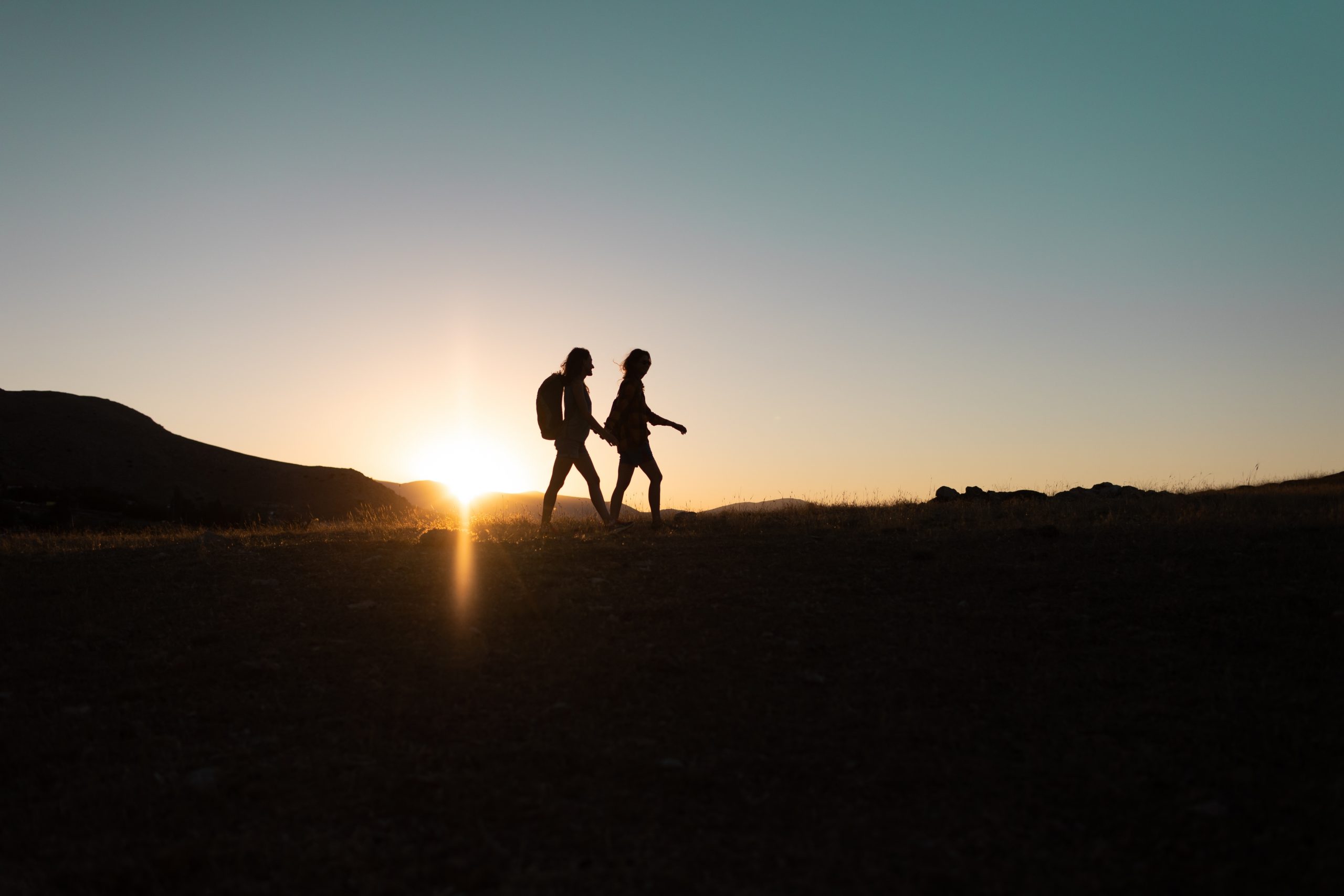 Silhouetted figures walking hand in hand against a vibrant sunset, with mountains in the background.