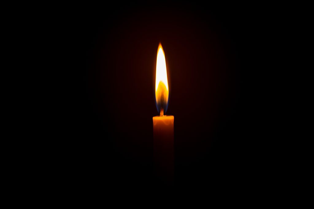 A single candle with a bright flame flickers against a dark background.