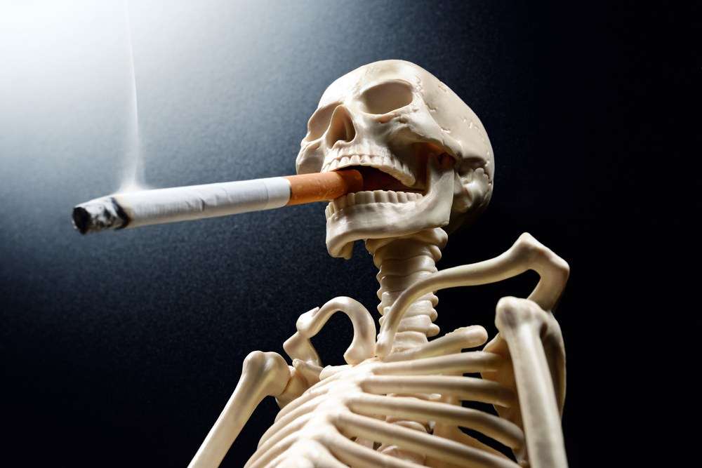 Skeleton holding a cigarette, exhaling smoke, set against a dark background with dramatic lighting.